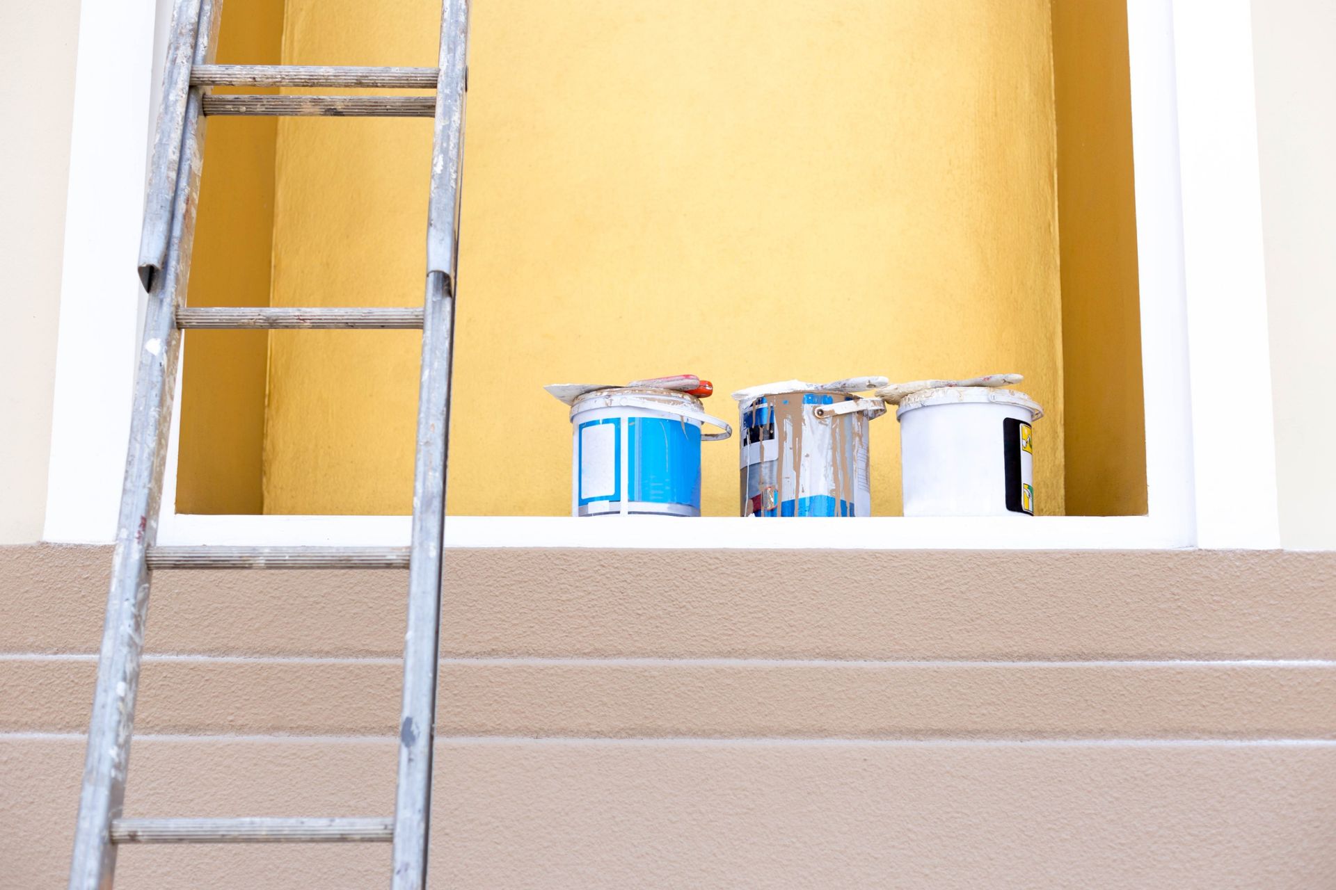 Hay tres cubos de pintura en el alféizar de una ventana, al lado de una escalera.