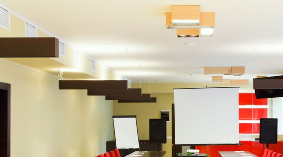 Sala de reuniones moderna con pantalla de proyector, pizarra blanca, sillas negras y paneles decorativos de pared rojos.