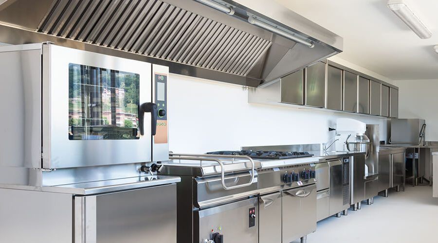Cocina comercial de acero inoxidable con amplia cocina, fregadero, armarios y campana extractora.