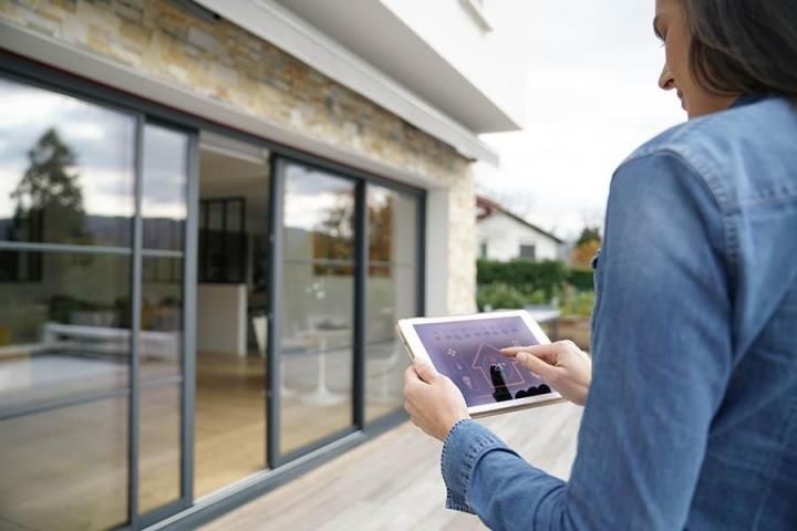 Personne tenant une tablette devant une maison moderne dotée de grandes baies vitrées