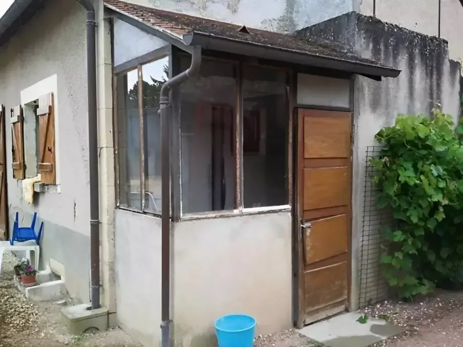 Petit abri de jardin avec une porte en bois, des fenêtres grillagées et un seau bleu à côté.