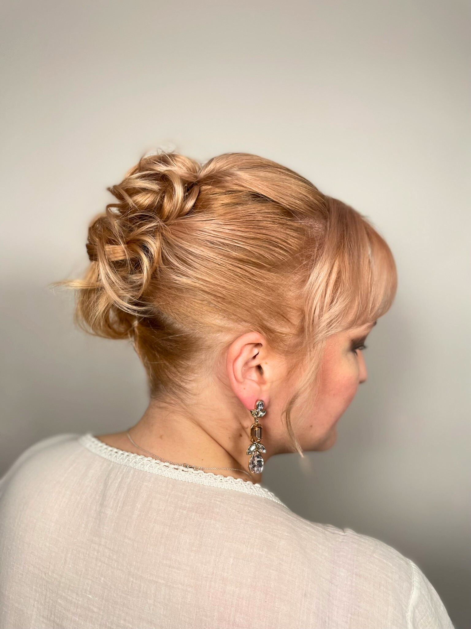 A woman wearing a white sweater and earrings has her hair in a bun