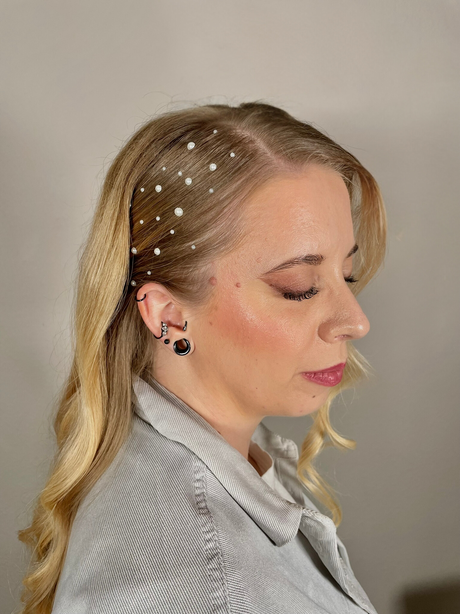 A woman with long blonde hair and earrings is wearing a striped shirt.