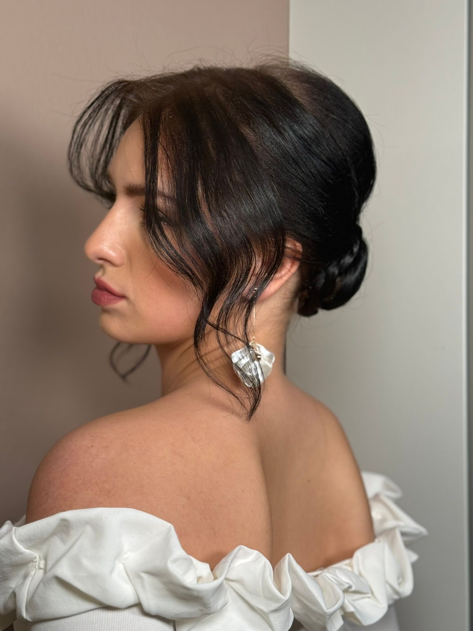 The woman is wearing a white off the shoulder top and earrings.