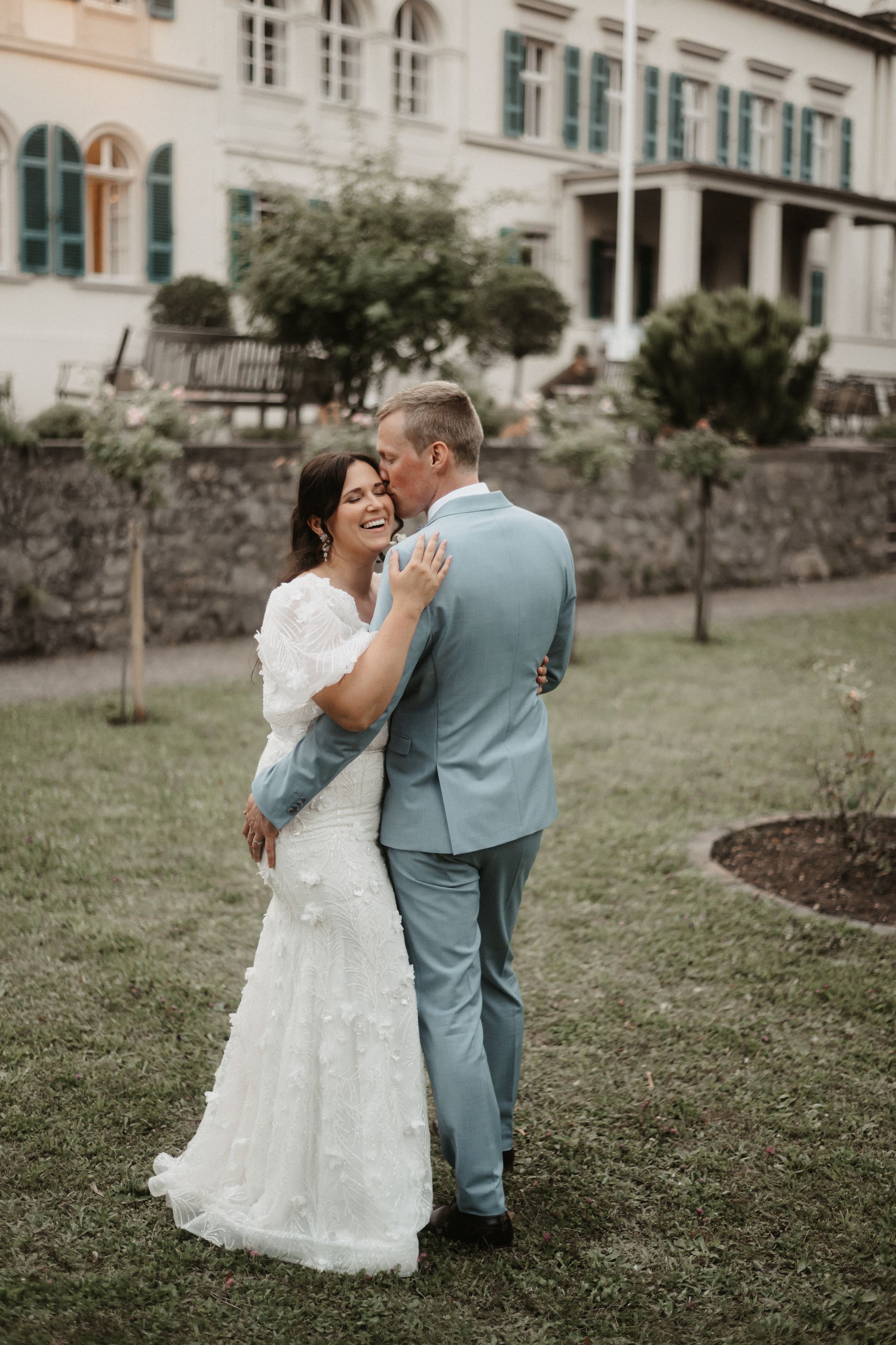 A bride and groom are dancing in a park in front of a building.