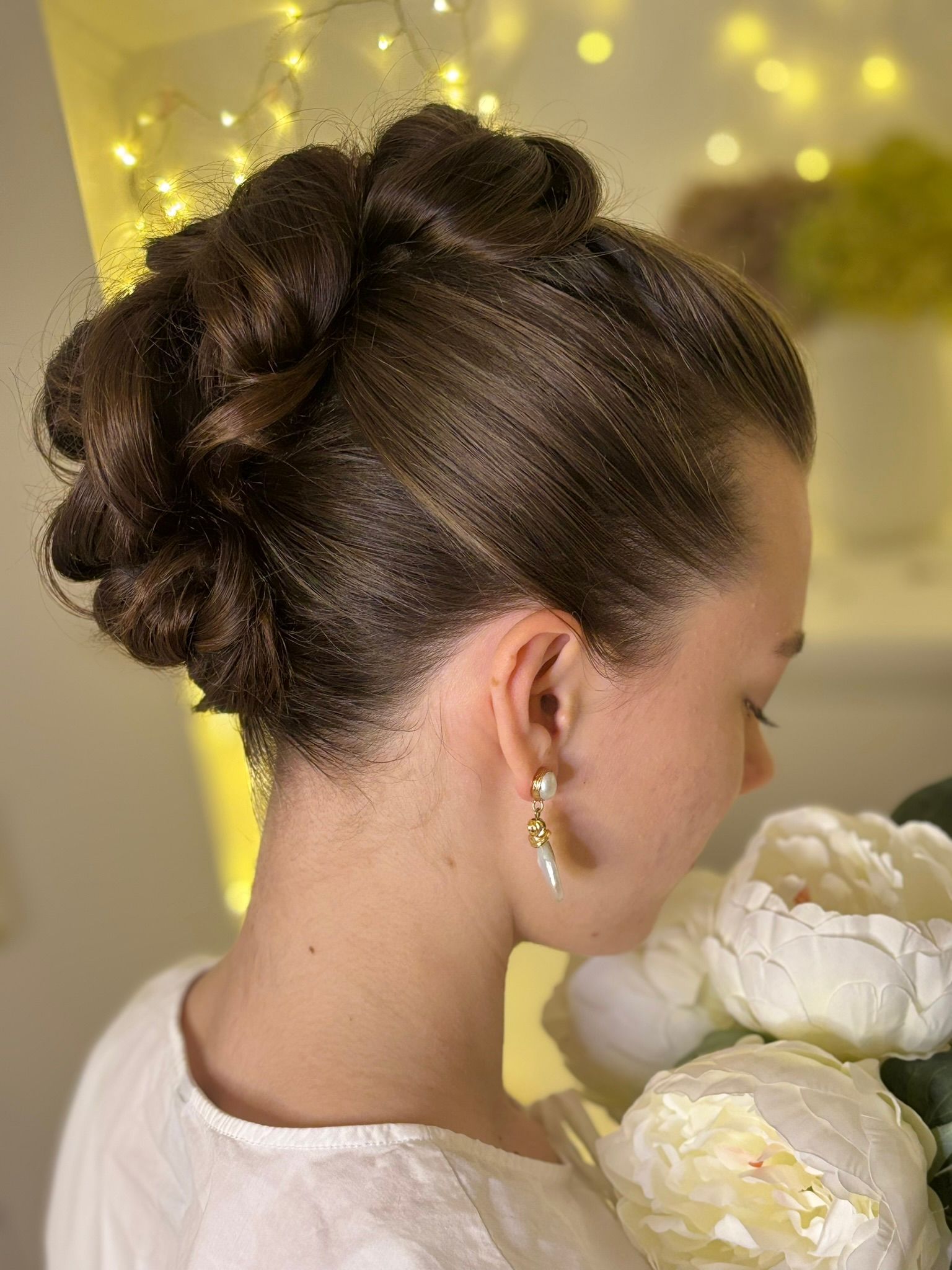 A woman with her hair in a bun is holding a bouquet of white flowers
