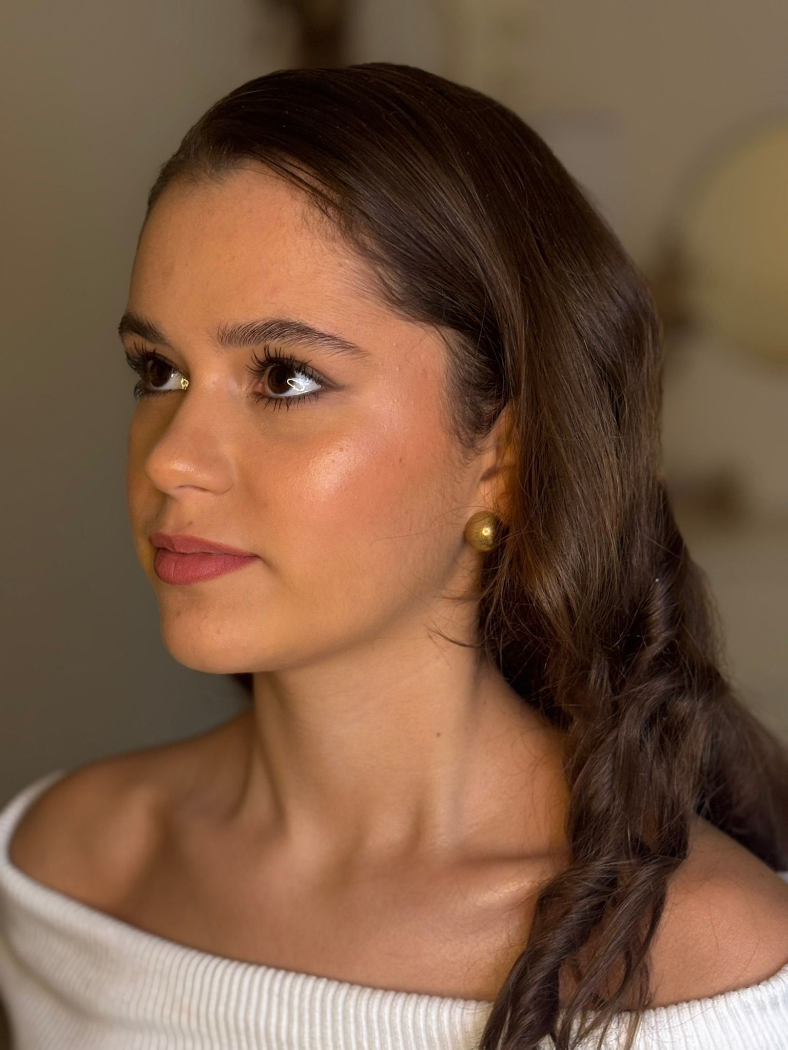 The woman is wearing a white off the shoulder top and earrings.