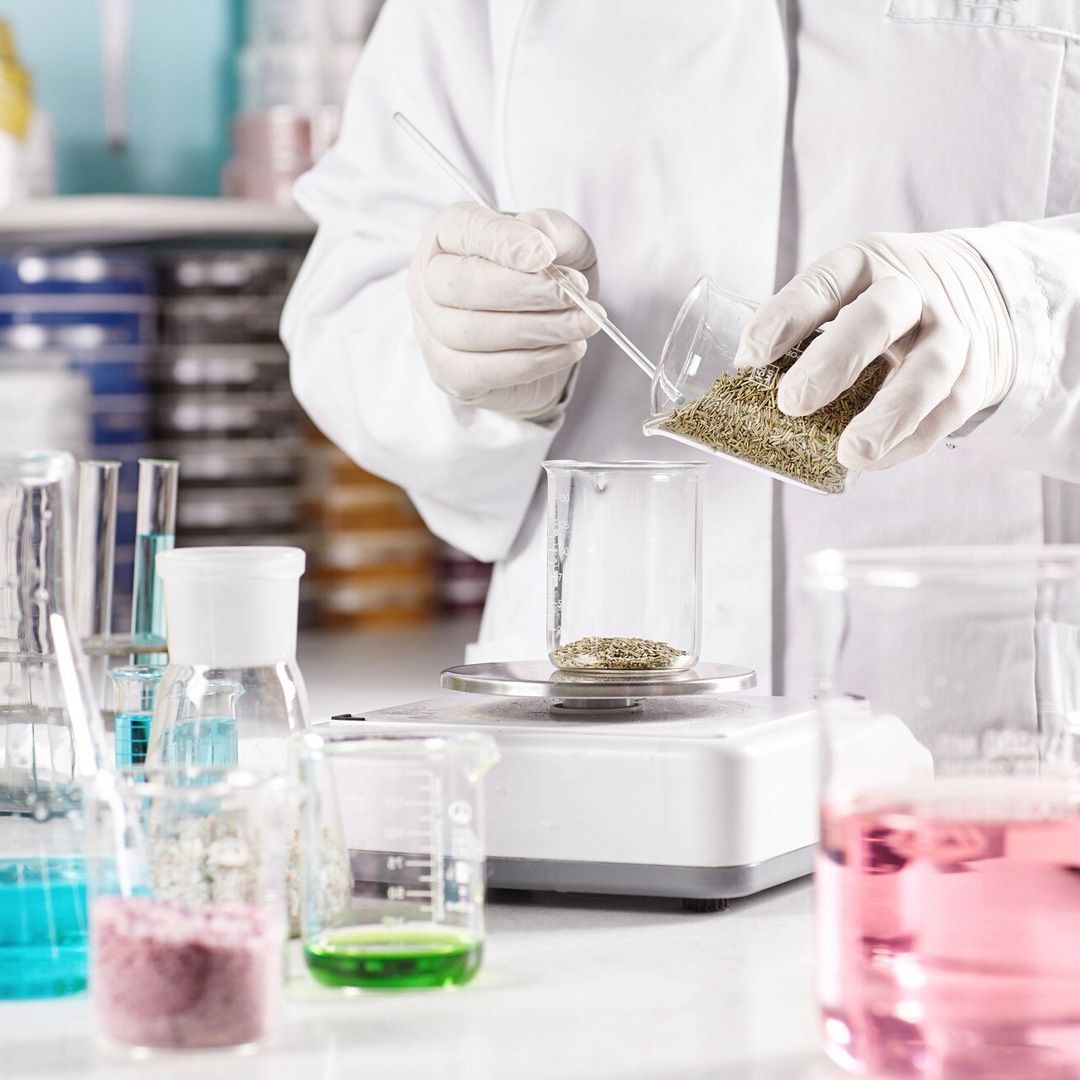 Tecnico di laboratorio versa un campione secco in un becher in un laboratorio con provette e vetreria colorate.