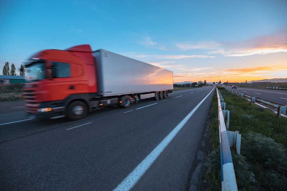 Un camión semirremolque rojo circula por una autopista al atardecer.