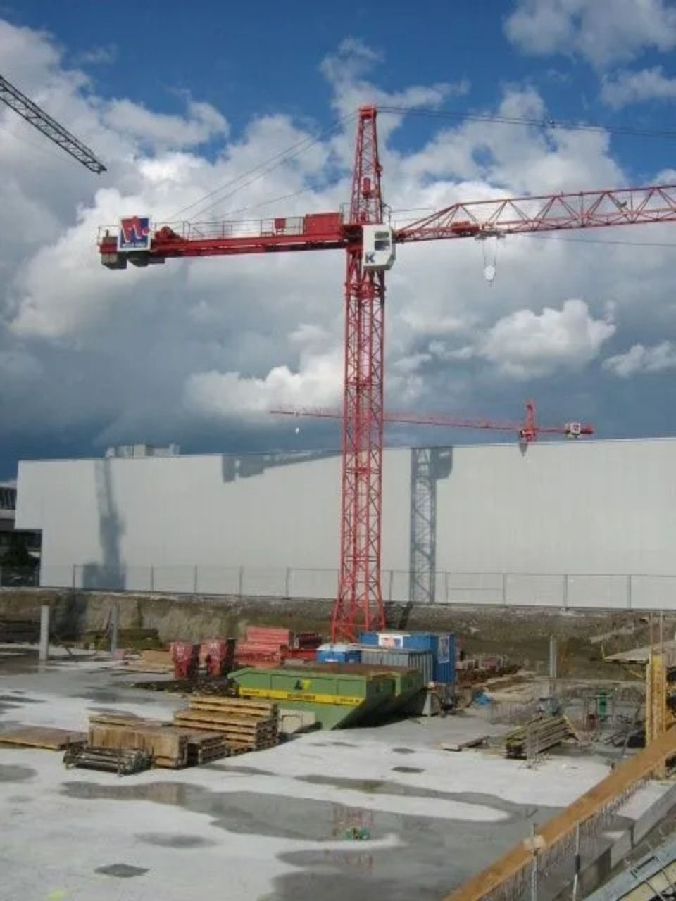 Über einer Baustelle mit einer weissen Mauer und verstreuten Baumaterialien ragt ein hoher roter Baukran empor.