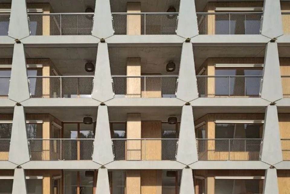 Eine gitterförmige Gebäudefassade mit modularen, beigefarbenen Paneelen, Balkonen mit Geländern und Betonstützen.