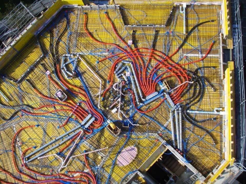 Luftbild einer Baustelle, auf der elektrische Leitungen in Rot, Blau und Schwarz über gelbe Schalungselemente verlegt sind.