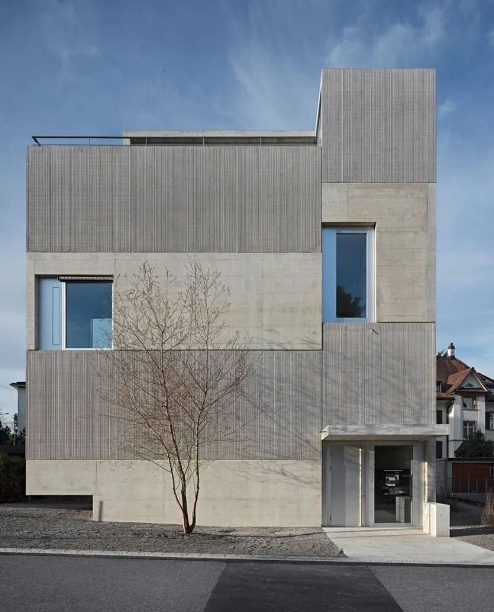 Ein modernes dreistöckiges Gebäude mit abwechselnden Abschnitten aus horizontaler Holzverkleidung und glatten Betonplatten unter freiem Himmel.