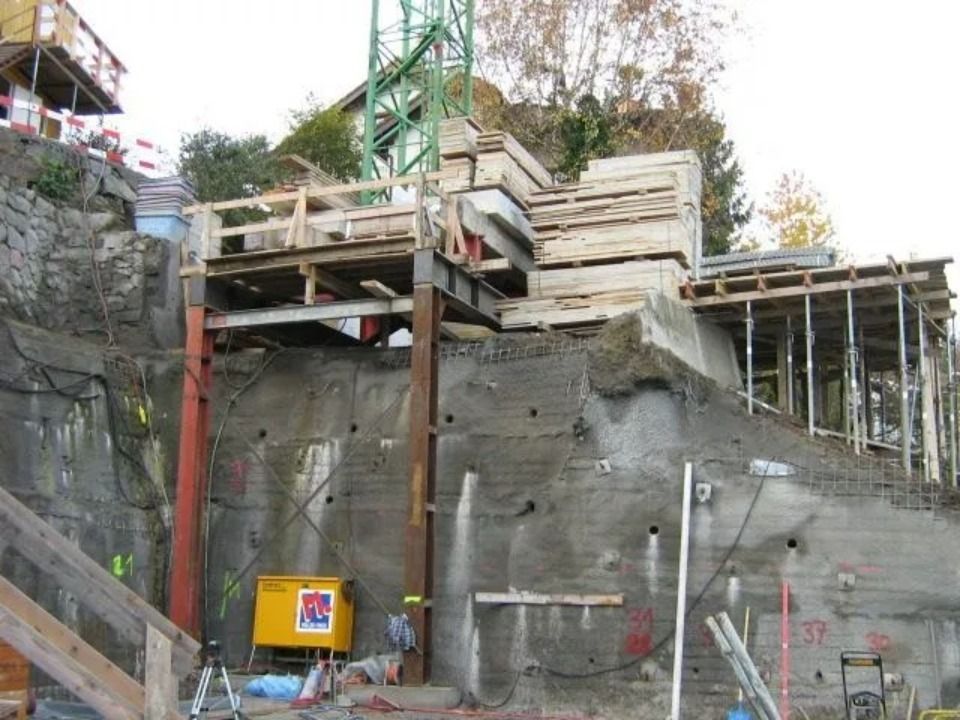 Baustelle mit einer stahlgestützten Plattform und einem Holzgerüst, das an einer felsigen Betonwand errichtet wurde.