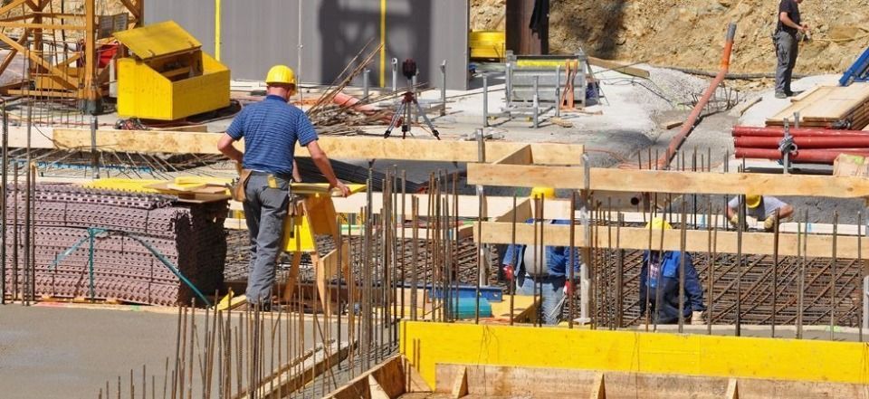 Bauarbeiter mit Schutzhelmen montieren auf einer Baustelle Holzschalungen und Metallarmierungen.