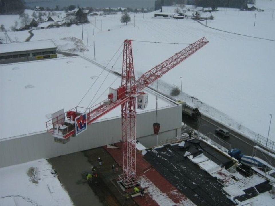 Auf einer schneebedeckten Baustelle steht ein roter Turmdrehkran neben einem weissen Gebäude.