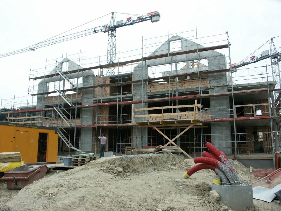 Baustelle mit einem mehrstöckigen Gebäudegerüst, einem Gerüst, einem hohen Kran und Erdhaufen im Vordergrund.