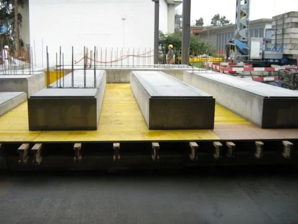 Auf einer gelben Schalungsplattform auf einer Baustelle liegen vorgefertigte Betonsegmente, die Bewehrungsstäbe sind sichtbar.