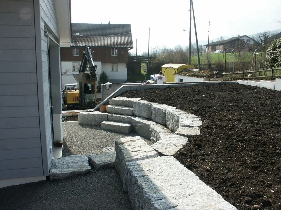 Ein neu gestalteter Hinterhof besticht durch geschwungene Stützmauern aus Granitblöcken und eine gestufte Steintreppe neben dem Haus.