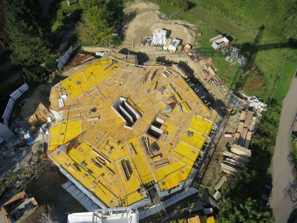 Luftaufnahme einer sechseckigen Baustelle mit gelben Schalungselementen auf einem Betonbodengerüst.