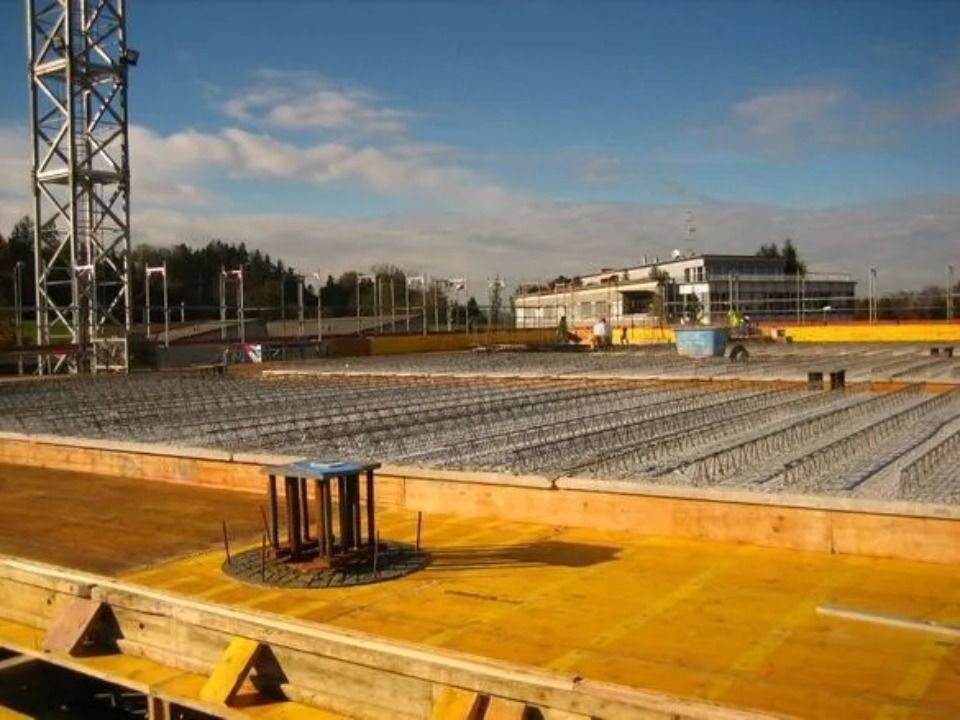 Eine Baustelle mit einer gelben Sperrholzschalung und einem Stahlbewehrungsgitter unter blauem, bewölktem Himmel.