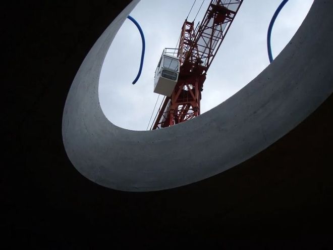 Auf einer Baustelle sind unter bewölktem Himmel Betonfundamentwände und Stützpfeiler auf ebenem Boden zu sehen.