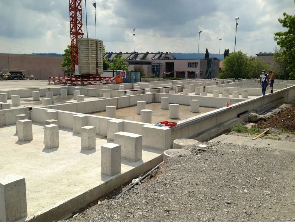 Eine Baustelle mit einer gelben Sperrholzschalung und einem Stahlbewehrungsgitter unter blauem, bewölktem Himmel.
