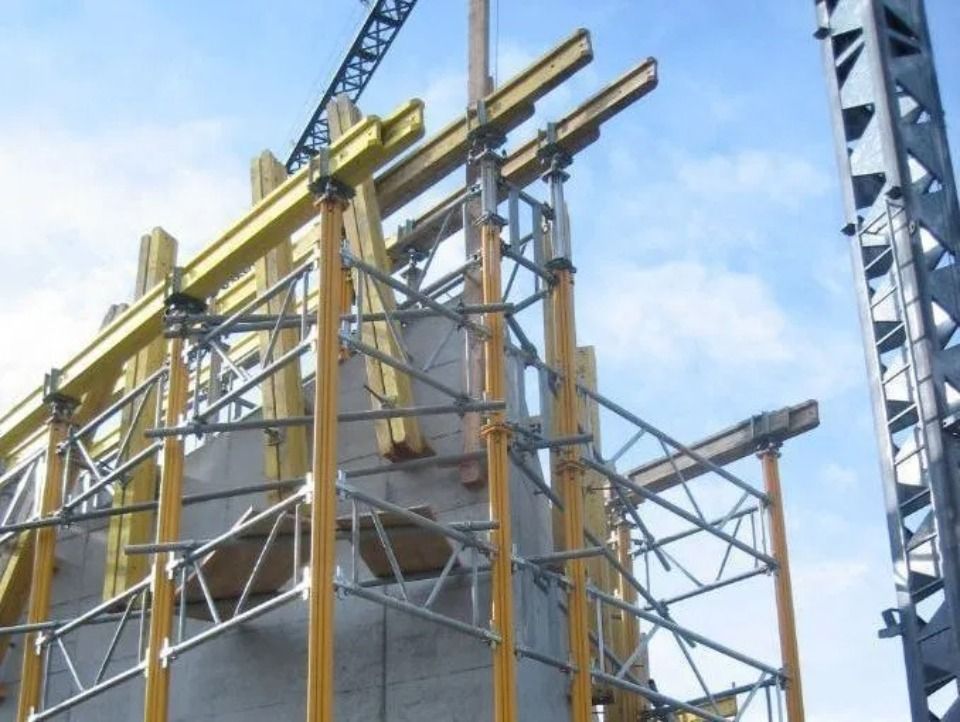 Gelbe Baugerüste und Stützbalken stützen eine Betonkonstruktion unter blauem Himmel.