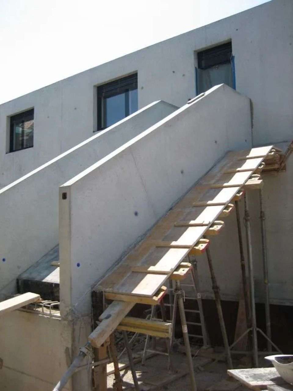 Eine im Bau befindliche Aussentreppe aus Beton, die von einer provisorischen Holzkonstruktion und Gerüstpfosten aus Metall getragen wird.