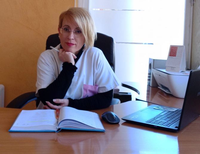 Una mujer se sienta en un escritorio con un libro y una computadora portátil.