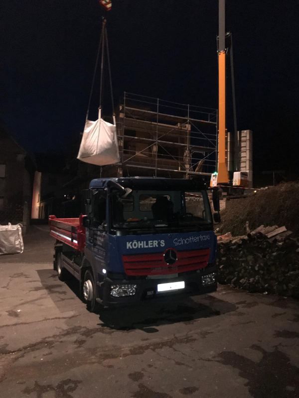 Kran entlädt Big Packs vom LKW in der Dunkelheit