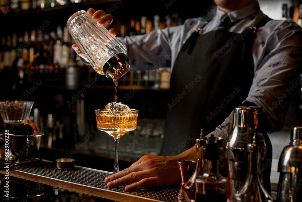 Ein Barkeeper schenkt in einer schwach beleuchteten Bar einen Cocktail in ein Glas ein.