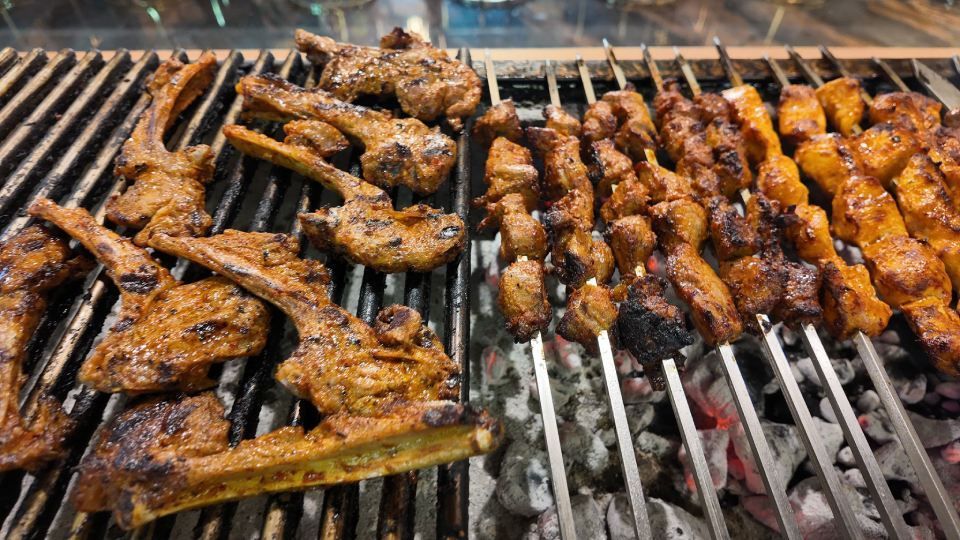 Verschiedene Fleischspiesse brutzeln über glühender Holzkohle auf einem Grill, mit angebrannten und glasierten Stücken.