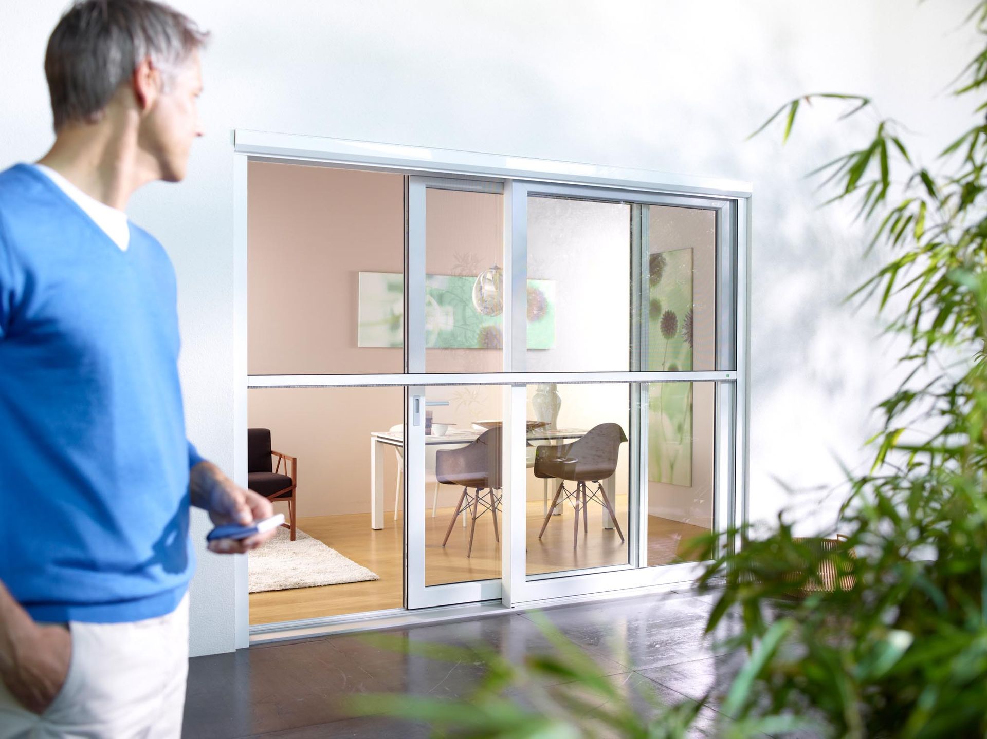 Ein Mann in einem blauen Pullover steht vor einer Glasschiebetür.