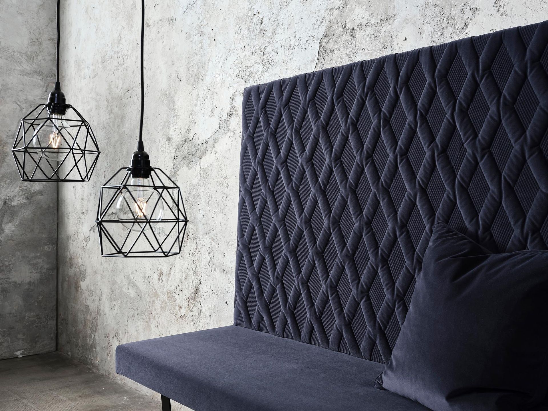 In einem Raum neben einer Betonwand steht ein blaues Sofa.