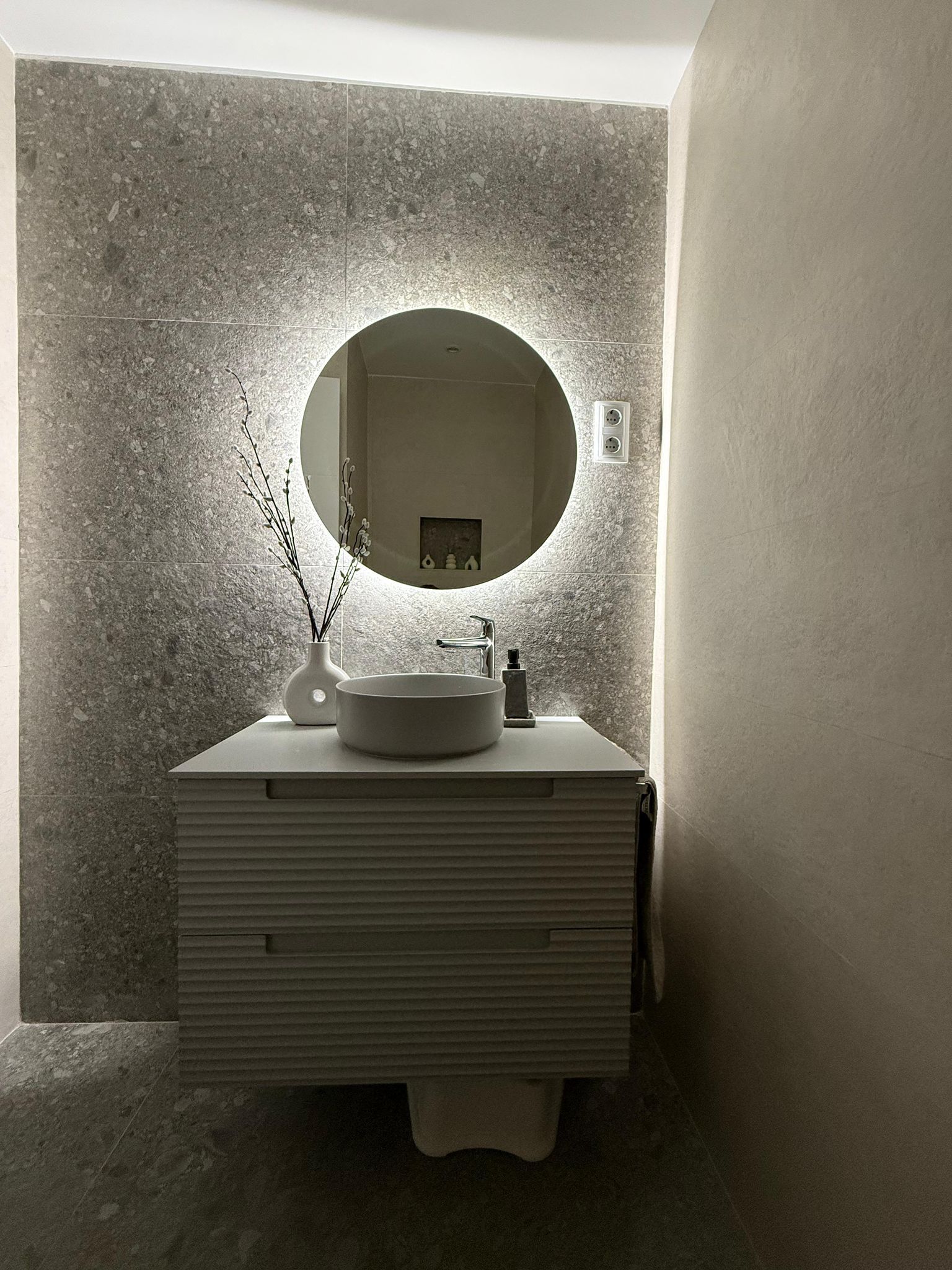 Un baño con lavabo y espejo redondo.