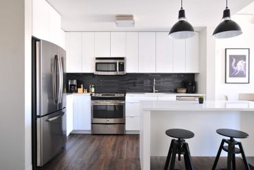 Una cocina con gabinetes blancos, electrodomésticos de acero inoxidable, refrigerador y microondas.