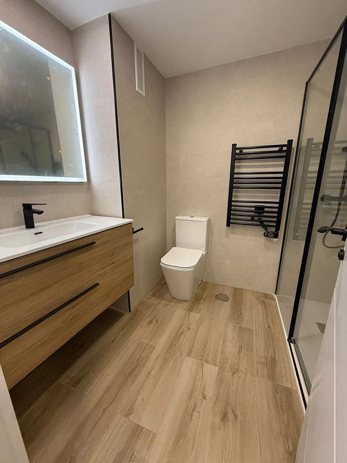 Baño moderno con tocador de madera, inodoro, ducha independiente y toallero.