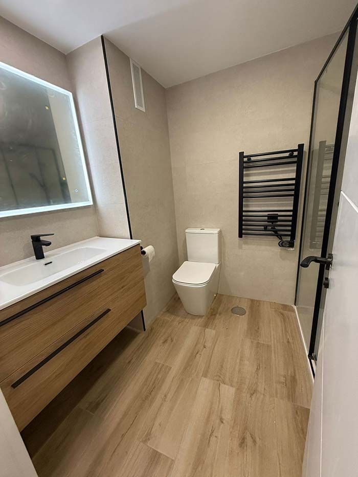 Baño moderno con tocador de madera, inodoro blanco, toallero y puerta de ducha de cristal.
