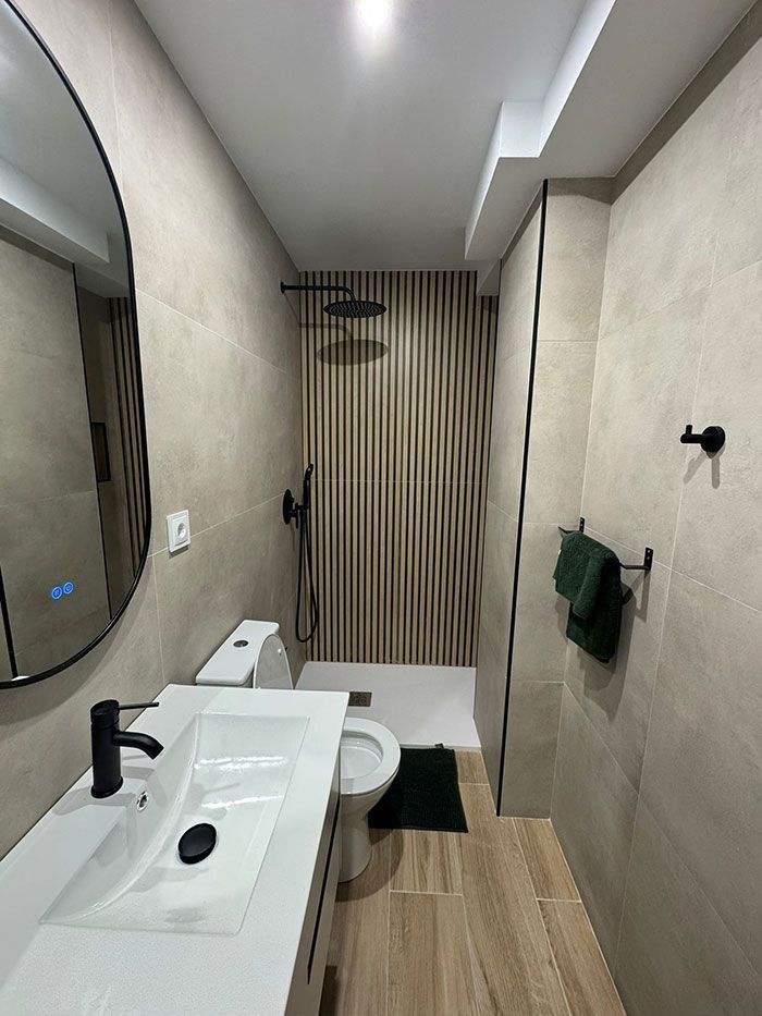 Baño moderno y estrecho con lavabo, inodoro, cortina de ducha y detalles de madera.