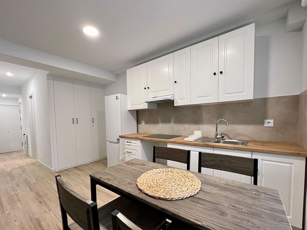 Cocina y comedor modernos con armarios blancos, encimeras de madera y sillas negras.