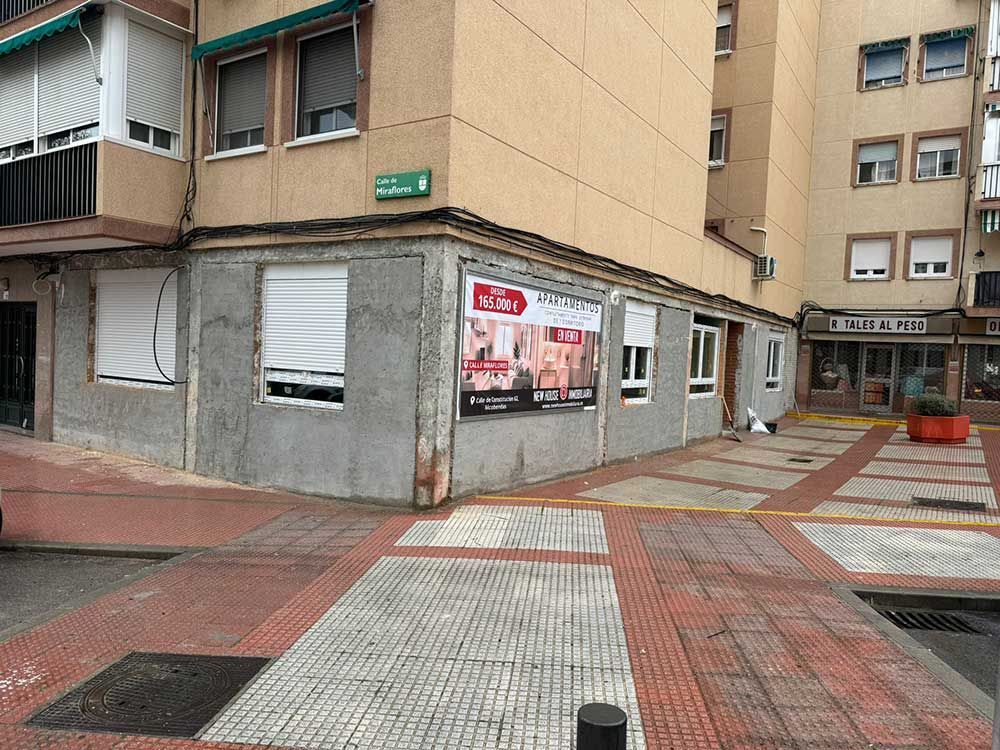 Esquina de un edificio de apartamentos con carteles publicitarios en el escaparate, acera de baldosas y entrada desde la calle.