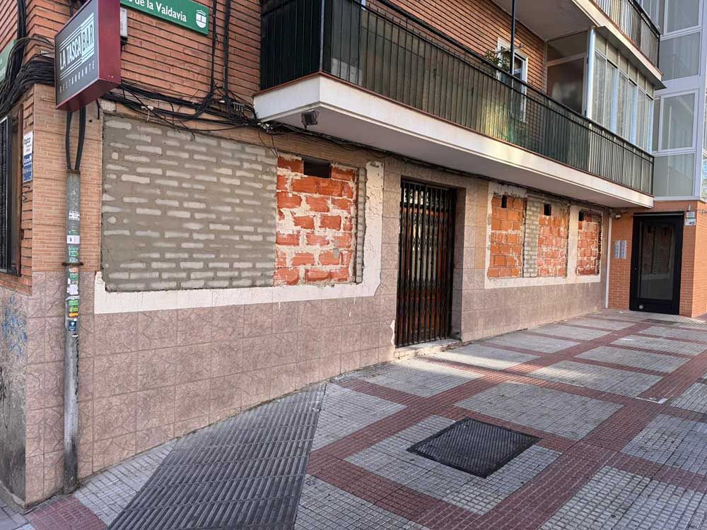 Fachada de un edificio de apartamentos a pie de calle con balcones, puerta enrejada y ventanas tapiadas, junto a una acera embaldosada.
