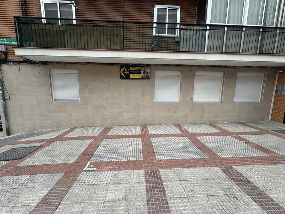 Patio exterior embaldosado con pavimento geométrico rojo y blanco frente a la fachada de un edificio y un balcón.