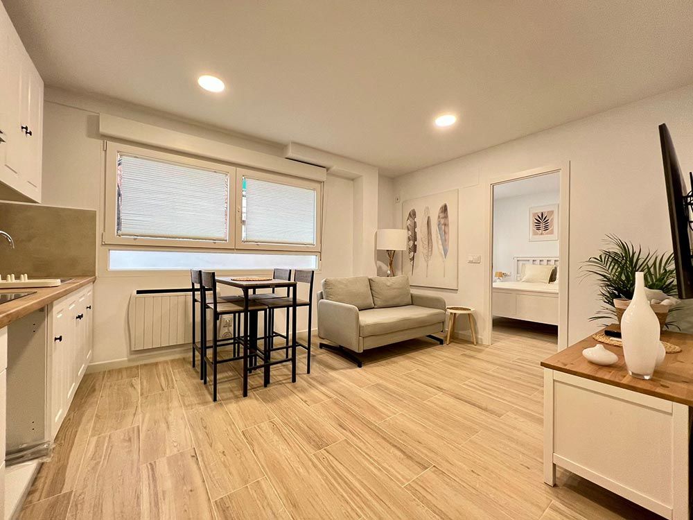 Estudio luminoso y moderno con sofá, mesa de comedor, suelos de madera y grandes persianas.
