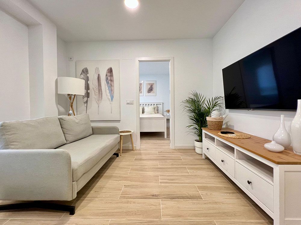 Luminoso salón moderno con sofá beige, televisor montado en la pared y consola blanca.