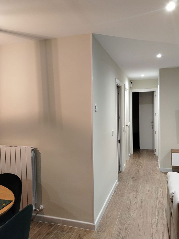 Pasillo moderno con suelos de madera clara, paredes beige, luces empotradas y una mesa de comedor en el extremo izquierdo.