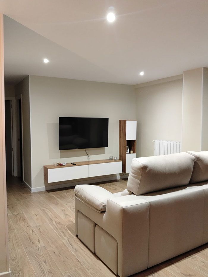 Salón moderno con sofá beige, televisor montado en la pared y suelo de madera clara.