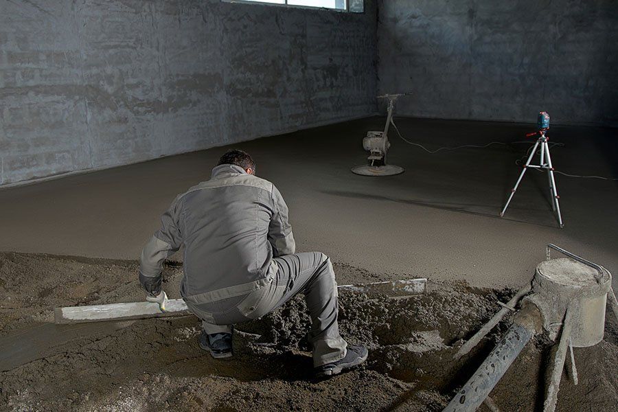 Un homme en train de lisser la mise en place d'une chape avec une règle
