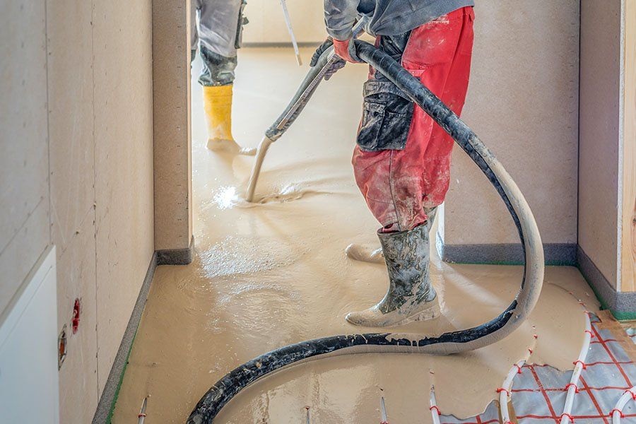 Des ouvriers sont en train de faire couler une chape fluide à l'aide d'un large tuyau noir